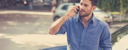 Junger Mann telefoniert mit seinem Handy an sein Auto gelehnt
